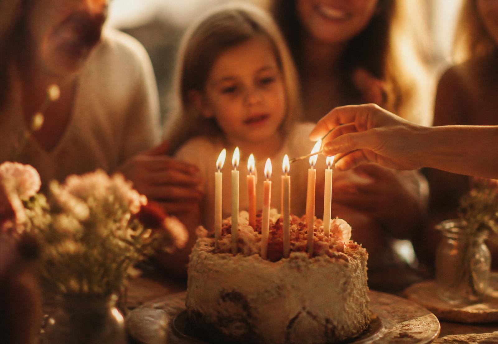 Candles being lit on a birthday cake with family in soft focus